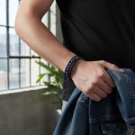 Avant-bras d'un homme portant un bracelet en cuir tressé noir avec perles de lapis-lazuli bleu et fermoir magnétique