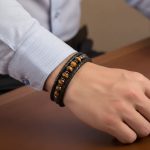Avant-bras d'un homme portant un bracelet en cuir tressé noir avec perles d'œil de tigre et fermoir magnétique