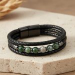 Bracelet homme en cuir tressé noir et agate mousse présenté sur bois clair avec éléments naturels