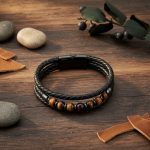 Bracelet homme en cuir tressé noir et œil de tigre présenté sur bois foncé avec éléments naturels