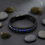 Bracelet homme en cuir tressé noir et lapis-lazuli présenté sur pierre d'ardoise avec éléments naturels