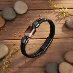 Bracelet homme en cuir tressé noir et perle d'agate marron présenté sur bois avec éléments naturels