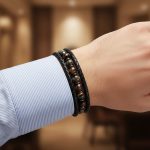 oignet d'un homme portant un bracelet en cuir tressé noir avec perles d'œil de tigre foncé et fermoir magnétique