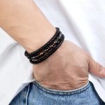 Poignet d'un homme dans la poche portant un bracelet en cuir tressé noir avec perles d'œil de tigre foncé