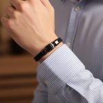 Poignet d'un homme portant un bracelet en cuir tressé noir avec perles de pierre de lave et fermoir magnétique