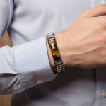 Poignet d'un homme portant un bracelet en cuir plat marron avec plaque en œil de tigre et fermoir magnétique acier