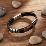 Bracelet homme en cuir plat marron et plaque d'œil de tigre avec acier argenté présenté sur bois