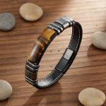 Bracelet homme en cuir plat noir et plaque d'œil de tigre présenté sur bois avec éléments naturels