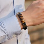 Poignet d'un homme portant un bracelet en cuir plat noir avec plaque en œil de tigre et fermoir magnétique noir et or
