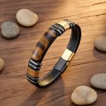 Bracelet homme en cuir plat noir et plaque d'œil de tigre avec acier noir et or présenté sur bois