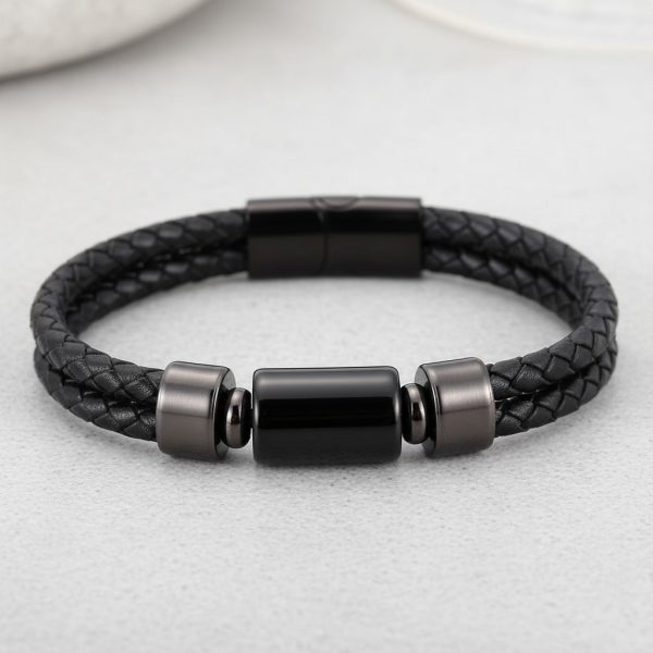 Gros plan d'un bracelet homme en cuir tressé noir avec perle cylindrique en acier noir sur fond pierre claire