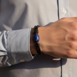 Poignet d'un homme portant un bracelet en cuir tressé noir avec perle centrale en lapis-lazuli et fermoir magnétique