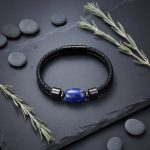 Bracelet homme en cuir tressé noir et perle de lapis-lazuli présenté sur ardoise avec éléments naturels