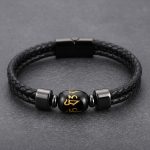 Gros plan d'un bracelet homme en cuir tressé noir avec perle d'obsidienne gravée mantra doré sur fond pierre sombre