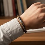 Poignet d'un homme portant un bracelet élastique en rondelles d'œil de tigre et hématite argentée