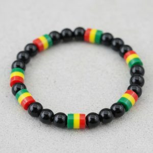 Gros plan d'un bracelet en perles noires brillantes avec perles rasta vert jaune rouge sur fond pierre claire