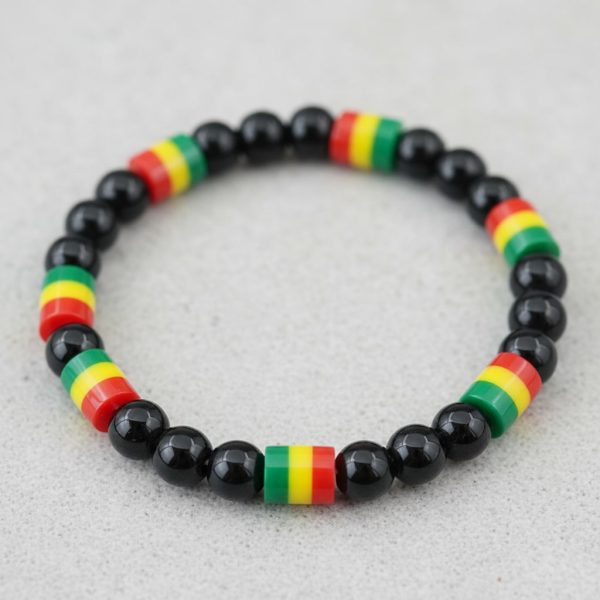 Gros plan d'un bracelet en perles noires brillantes avec perles rasta vert jaune rouge sur fond pierre claire