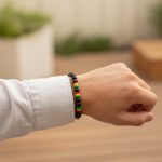 Poignet d'un homme portant un bracelet élastique en perles noires avec perles rasta vert jaune rouge