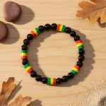 Bracelet en perles noires et perles rasta vert jaune rouge présenté sur bois naturel
