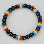 Gros plan d'un bracelet en perles noires brillantes avec perles tricolores bleu jaune rouge sur fond pierre claire
