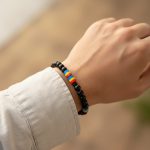 Poignet d'un homme portant un bracelet élastique en perles noires avec perles tricolores bleu jaune rouge