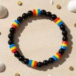 Bracelet en perles noires et perles tricolores bleu jaune rouge présenté sur bois clair