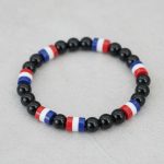 Gros plan d'un bracelet en perles noires brillantes avec perles tricolores bleu blanc rouge sur fond pierre claire
