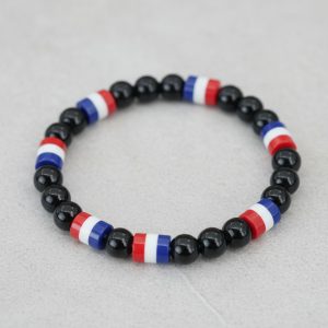 Gros plan d'un bracelet en perles noires brillantes avec perles tricolores bleu blanc rouge sur fond pierre claire