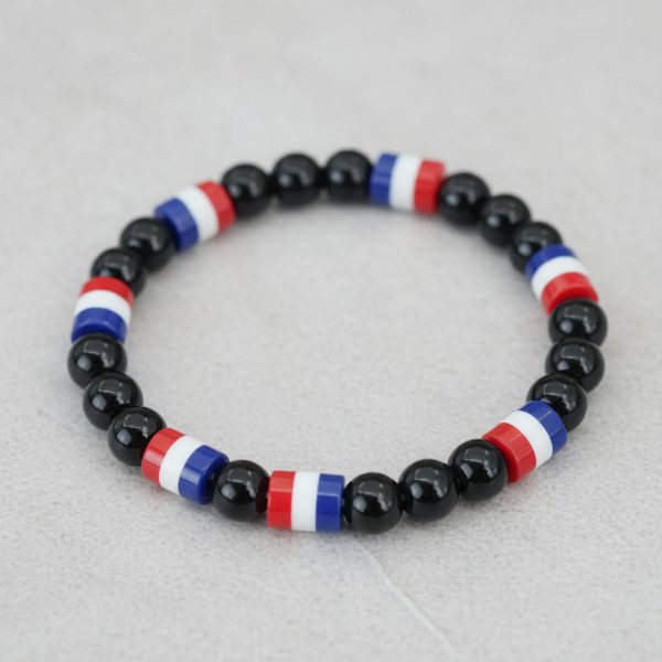 Gros plan d'un bracelet en perles noires brillantes avec perles tricolores bleu blanc rouge sur fond pierre claire