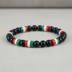 Gros plan d'un bracelet en perles noires brillantes avec perles tricolores vert blanc rouge sur fond pierre claire