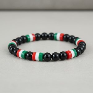 Gros plan d'un bracelet en perles noires brillantes avec perles tricolores vert blanc rouge sur fond pierre claire