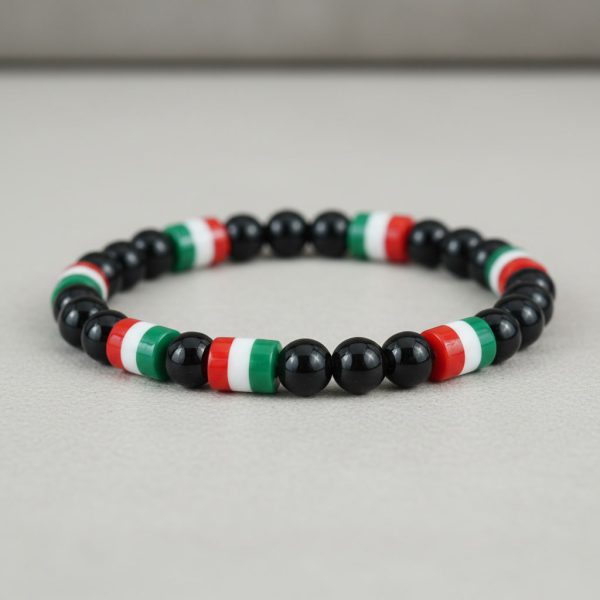 Gros plan d'un bracelet en perles noires brillantes avec perles tricolores vert blanc rouge sur fond pierre claire