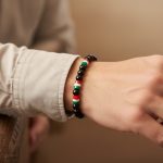 Poignet d'un homme portant un bracelet élastique en perles noires avec perles tricolores vert blanc rouge