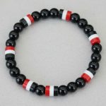 Gros plan d'un bracelet en perles noires brillantes avec perles tricolores noir blanc rouge sur fond pierre claire