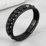 Gros plan d'un bracelet homme en cuir tressé noir avec perles de pierre de lave sur fond pierre claire