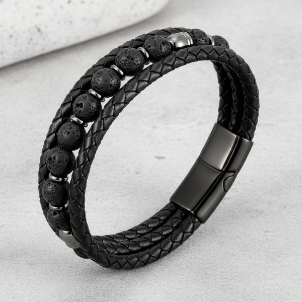 Gros plan d'un bracelet homme en cuir tressé noir avec perles de pierre de lave sur fond pierre claire