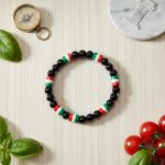 Bracelet en perles noires et perles tricolores vert blanc rouge présenté sur bois clair