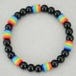 Gros plan d'un bracelet en perles noires brillantes avec perles arc-en-ciel sur fond pierre claire