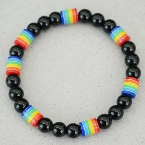 Gros plan d'un bracelet en perles noires brillantes avec perles arc-en-ciel sur fond pierre claire