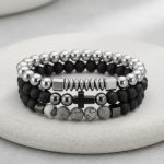 Gros plan d'un ensemble de trois bracelets homme en perles noires, hématite argentée et jaspe paysage gris sur fond pierre claire