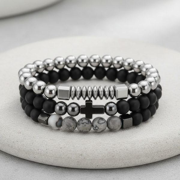 Gros plan d'un ensemble de trois bracelets homme en perles noires, hématite argentée et jaspe paysage gris sur fond pierre claire