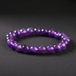 Gros plan d'un bracelet en perles d'améthyste violette translucide sur fond sombre