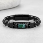 Gros plan d'un bracelet homme en cuir noir tressé et surpiqué avec tube en agate verte sur fond pierre claire