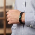 Poignet d'un homme portant un bracelet en cuir noir tressé et plat avec tube central en agate verte et fermoir magnétique
