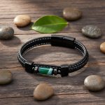 Bracelet homme en cuir noir et tube d'agate verte présenté sur bois foncé avec éléments naturels