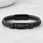 Gros plan d'un bracelet homme en cuir noir tressé et surpiqué avec tube en pierre de lave sur fond pierre claire