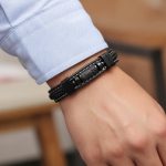 Poignet d'un homme portant un bracelet en cuir noir tressé et plat avec tube central en pierre de lave et fermoir magnétique