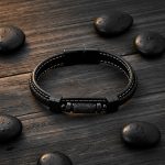 Bracelet homme en cuir noir et tube en pierre de lave présenté sur bois foncé avec éléments naturels
