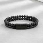 Gros plan d'un bracelet homme en cuir tressé noir et perles de pierre de lave sur fond pierre claire
