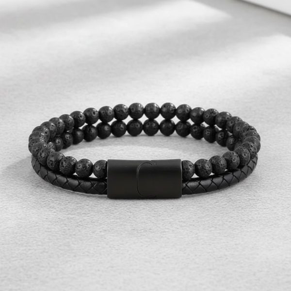 Gros plan d'un bracelet homme en cuir tressé noir et perles de pierre de lave sur fond pierre claire